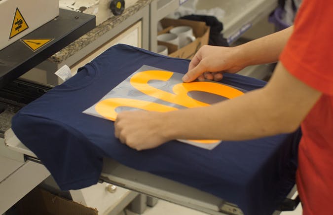 Pessoa colocando o adesivo em uma camiseta para estampar na técnica de Plotter