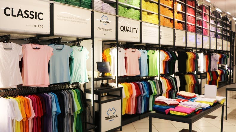 Interior da loja do Centro da Dimona, com várias camisas coloridas penduradas em araras