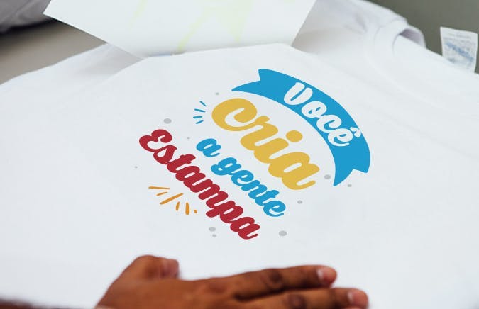 Banner com uma camisa personalizada pela técnica de estamparia Transfer, escrito "você cria, a gente estampa"