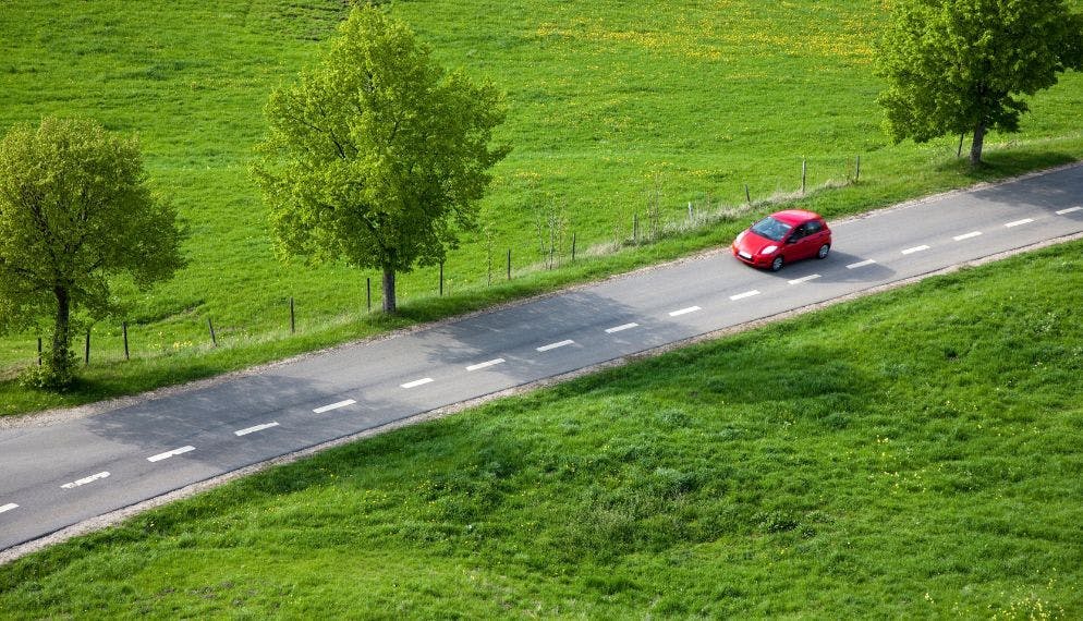 Petite voiture rouge conduit sur une route de campagne en vue aérienne