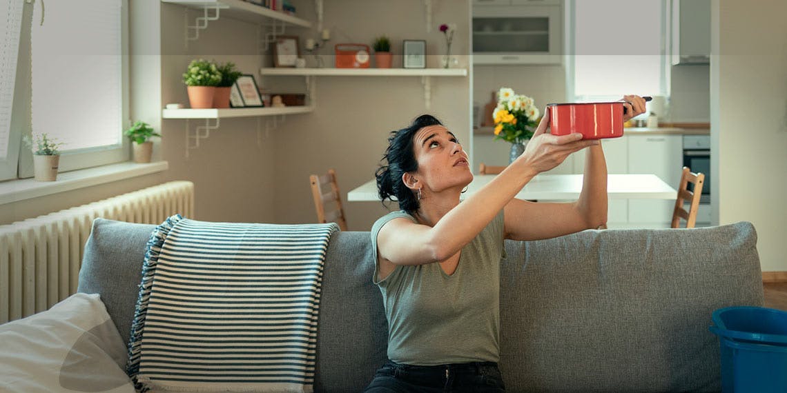 femme sur canapé avec casserole dégât des eaux provenant du plafond