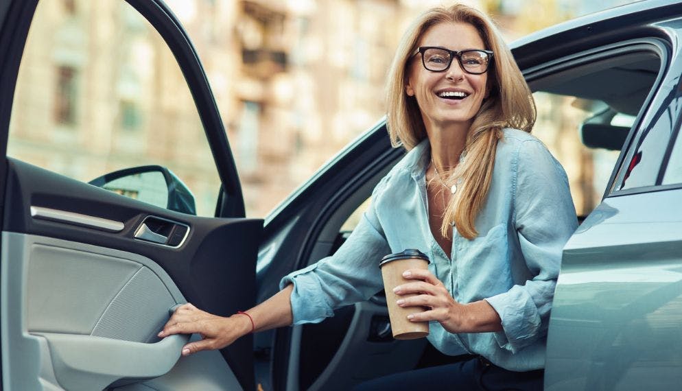 Une femme tenant une tasse sort de sa voiture