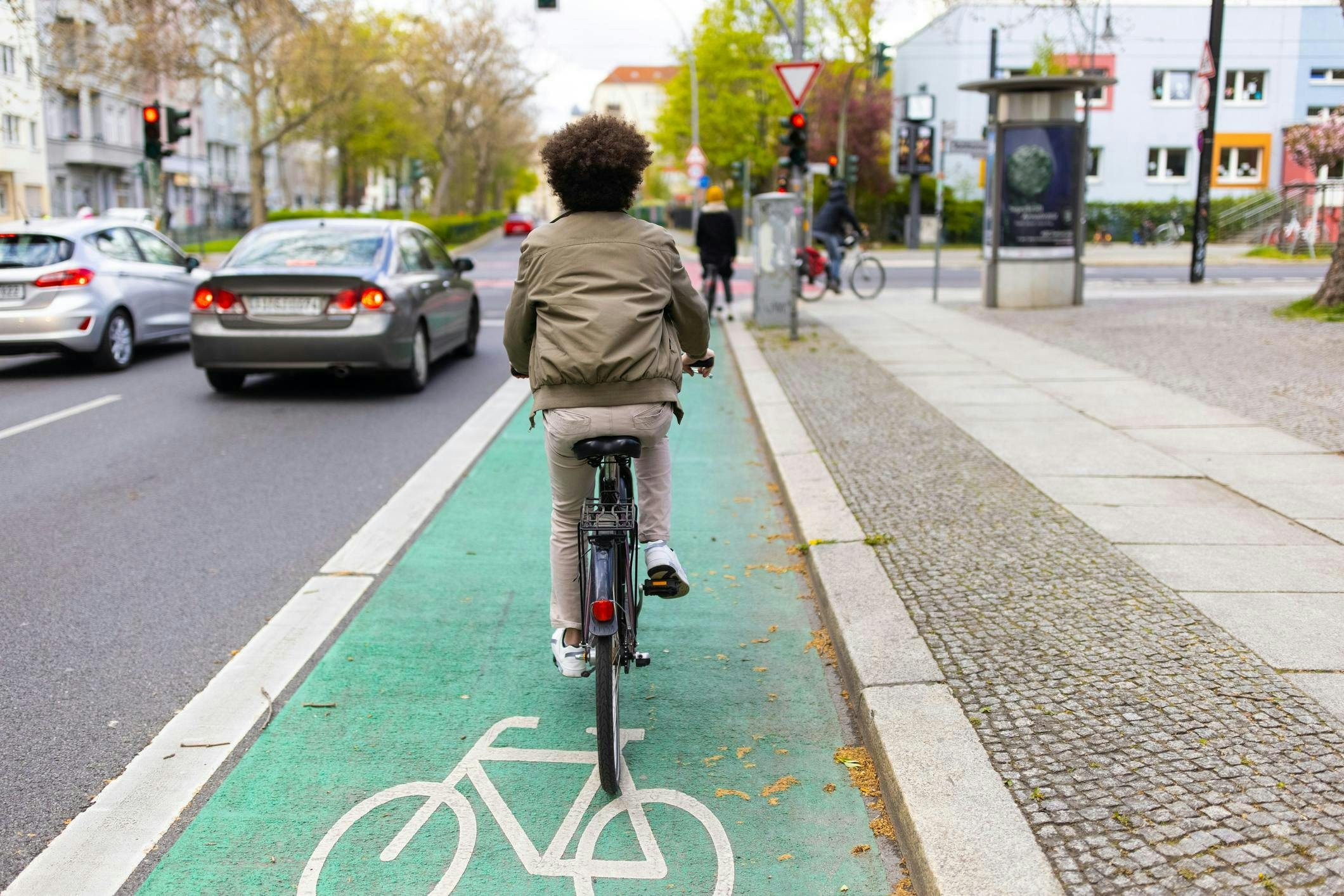 un jeune homme fait du vélo sur une piste cyclable en ville entouré de voitures