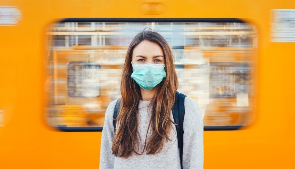 une jeune femme masquée devant un train orange