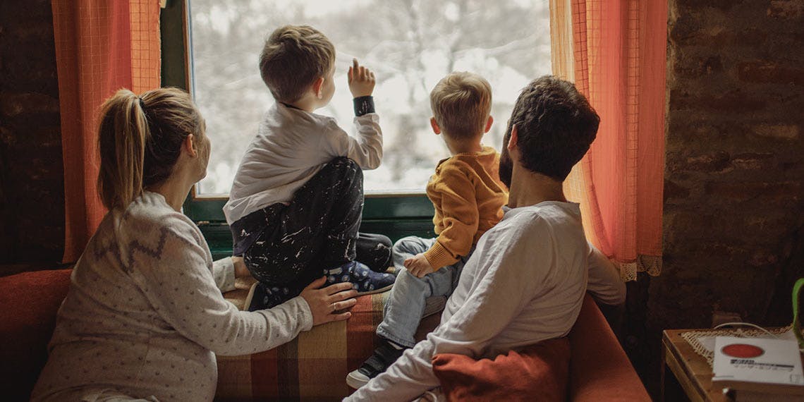 famille regardant la neige derrière la fenêtre