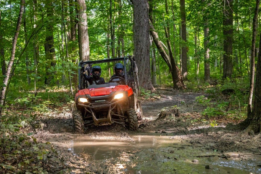 2025 Honda Pioneer 700 coming around a muddy corner.