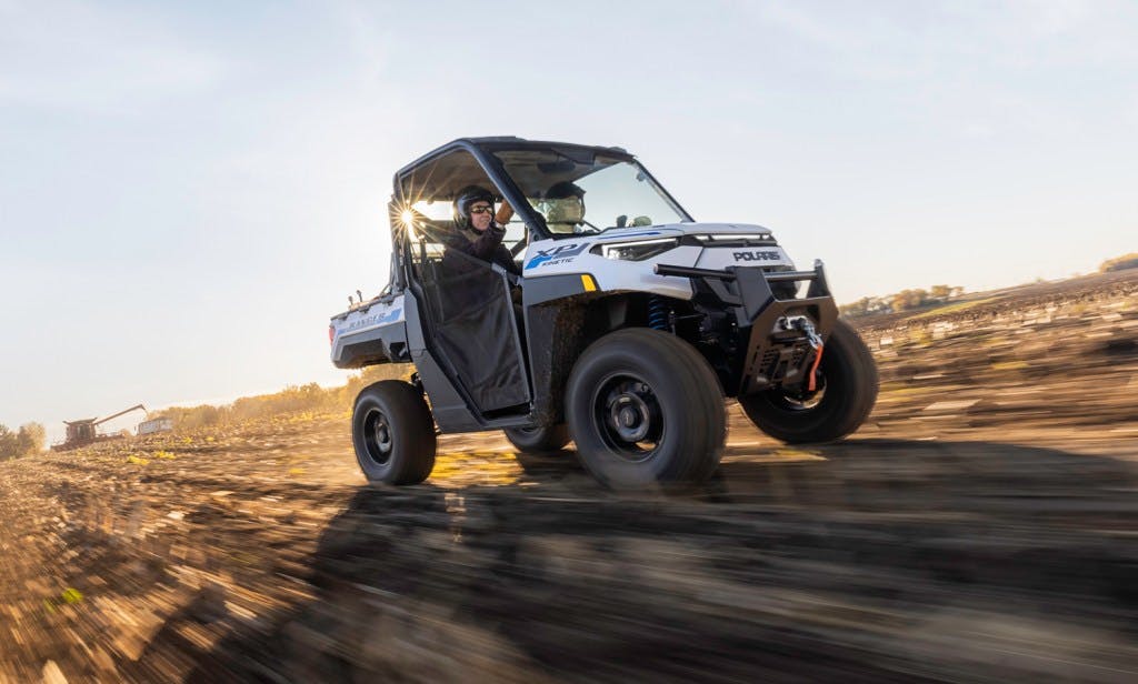 2024 Polaris Ranger Kinetic EV running through a field with the sun behind it