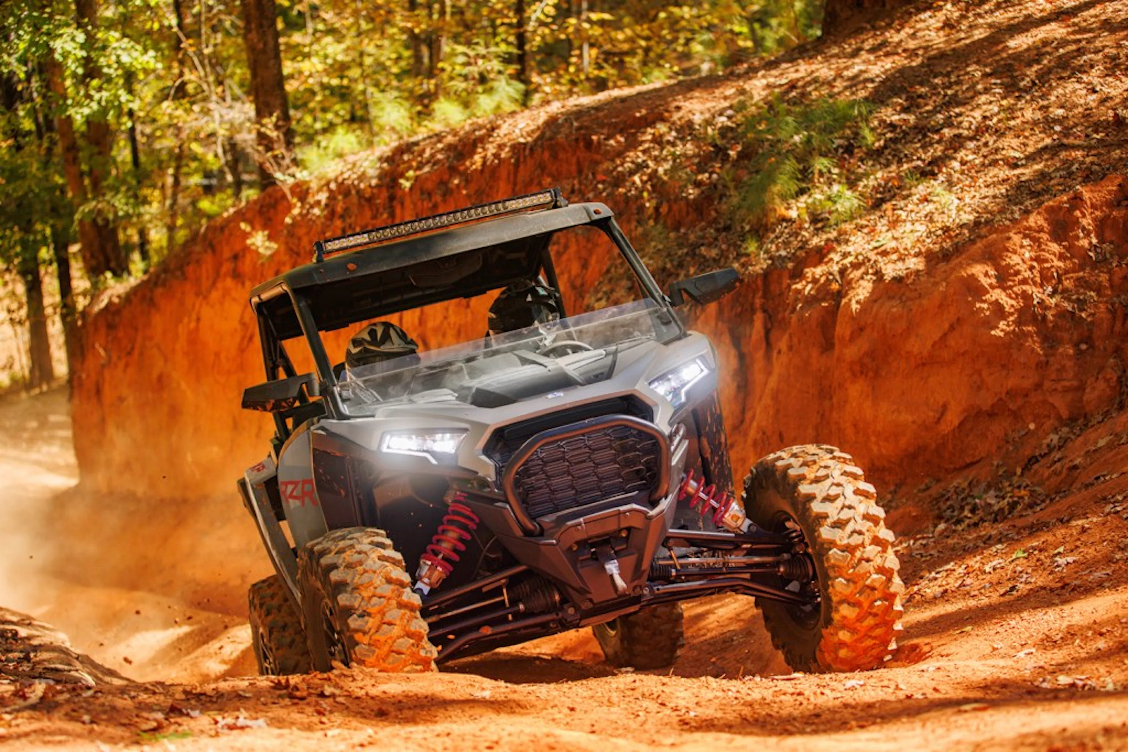 2025 Polaris RZR XP Premium climbing a muddy dirty hill headlights on