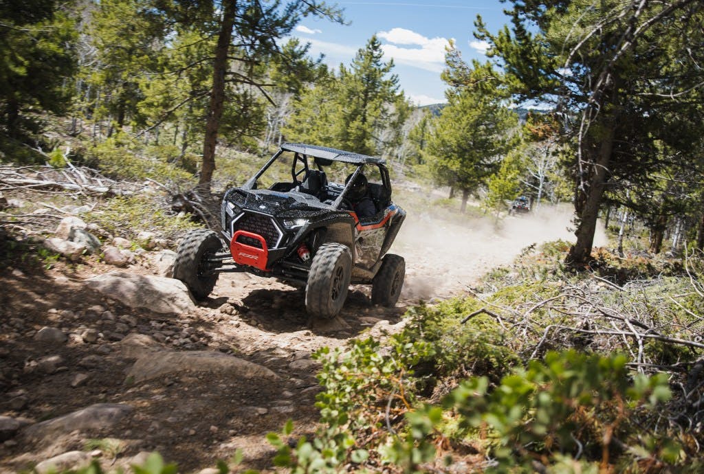 2025 Polaris RZR Pro XP Ultimate Onyx in the woods accelerating up a hill wheel in air