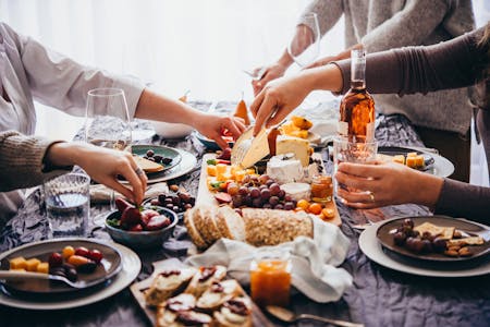 People eating at a restaurant table with a spread of good available and a bottle of wine