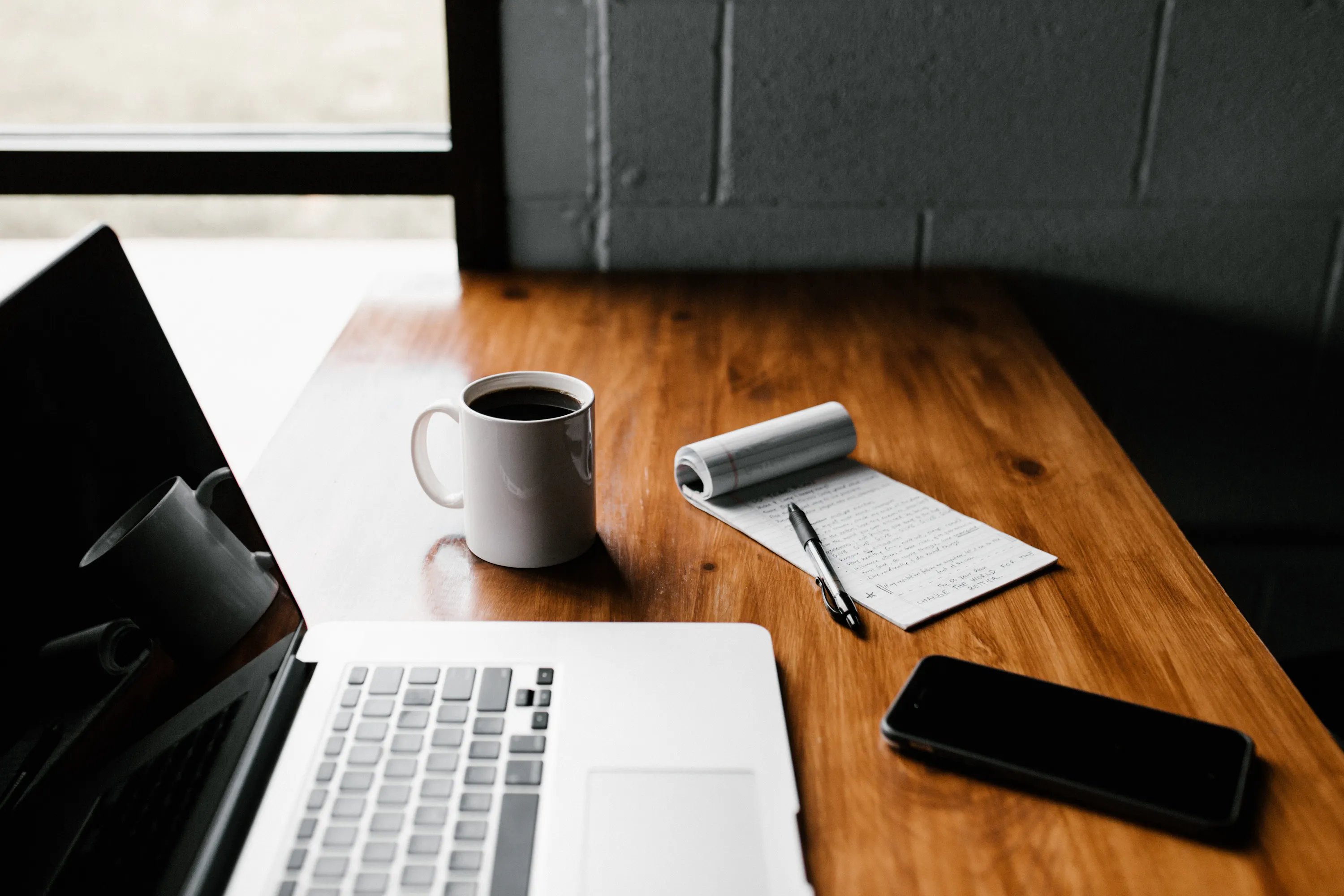 desk setting with coffee, computer, pen, paper, and phone