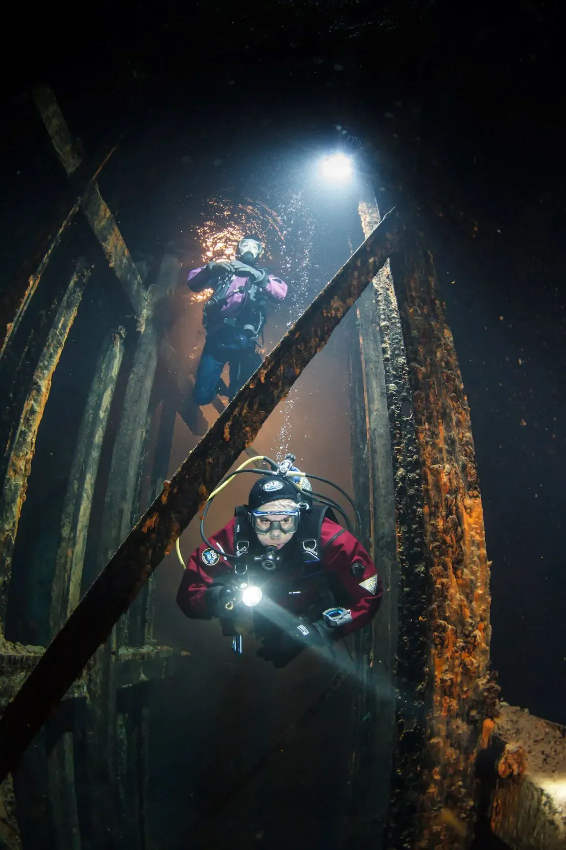 Two scuba divers scuba diving inside a ship wreck.