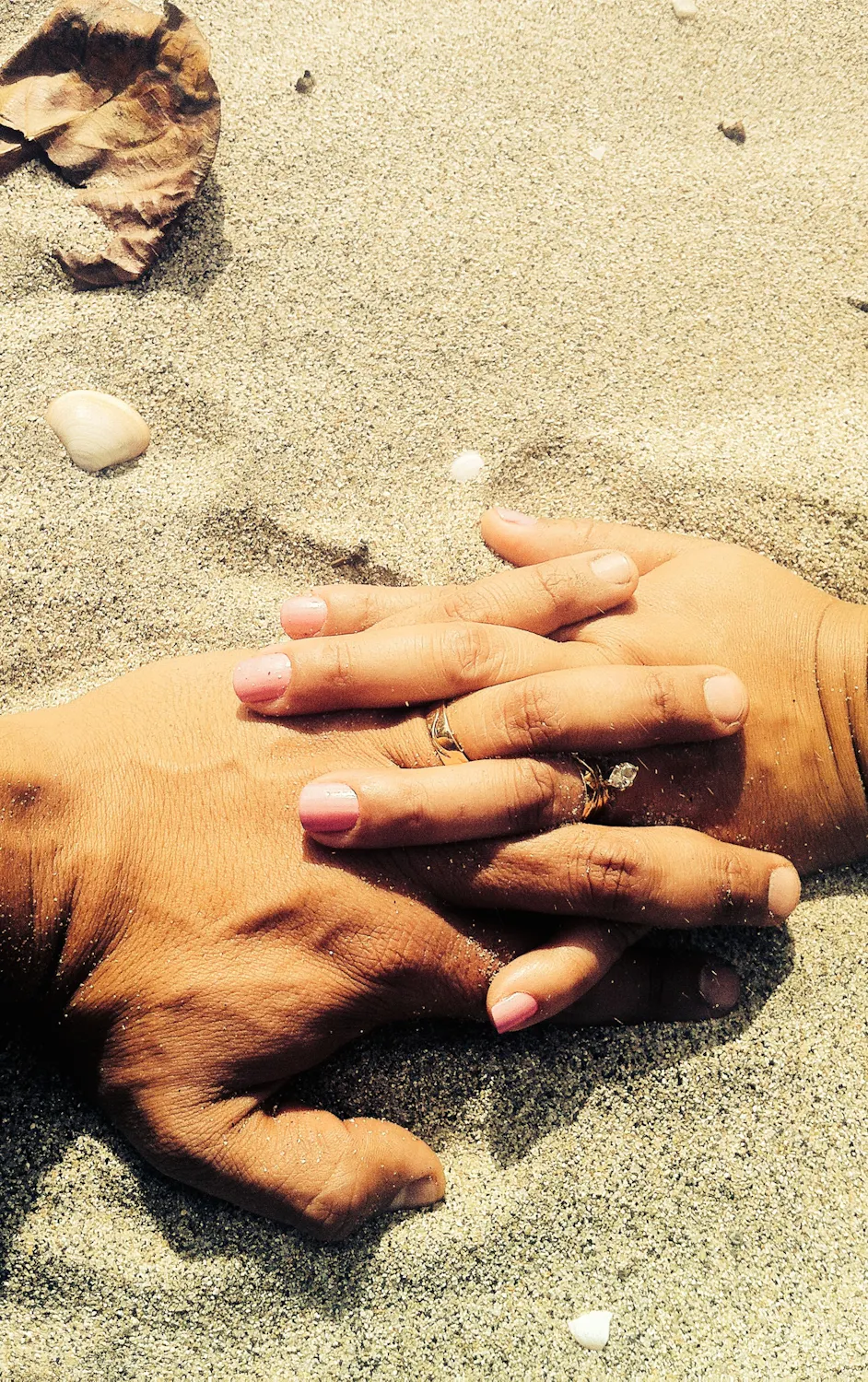 two different hands interlocked laying on sand