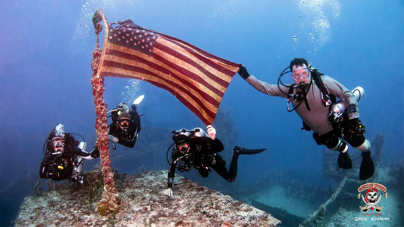 Four scuba divers posing underwater at the Spiegel Grove's American flag