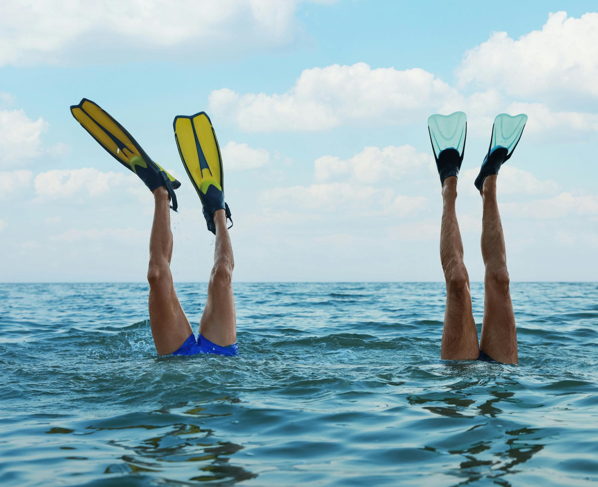 Two divers with their legs above the ocean's surface with fins on