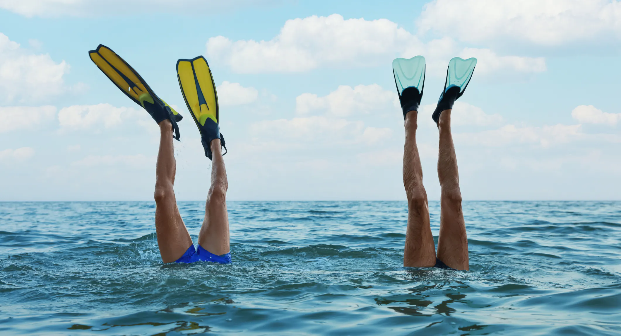 two swimmers with fins on. Only the legs above the ocean's surface
