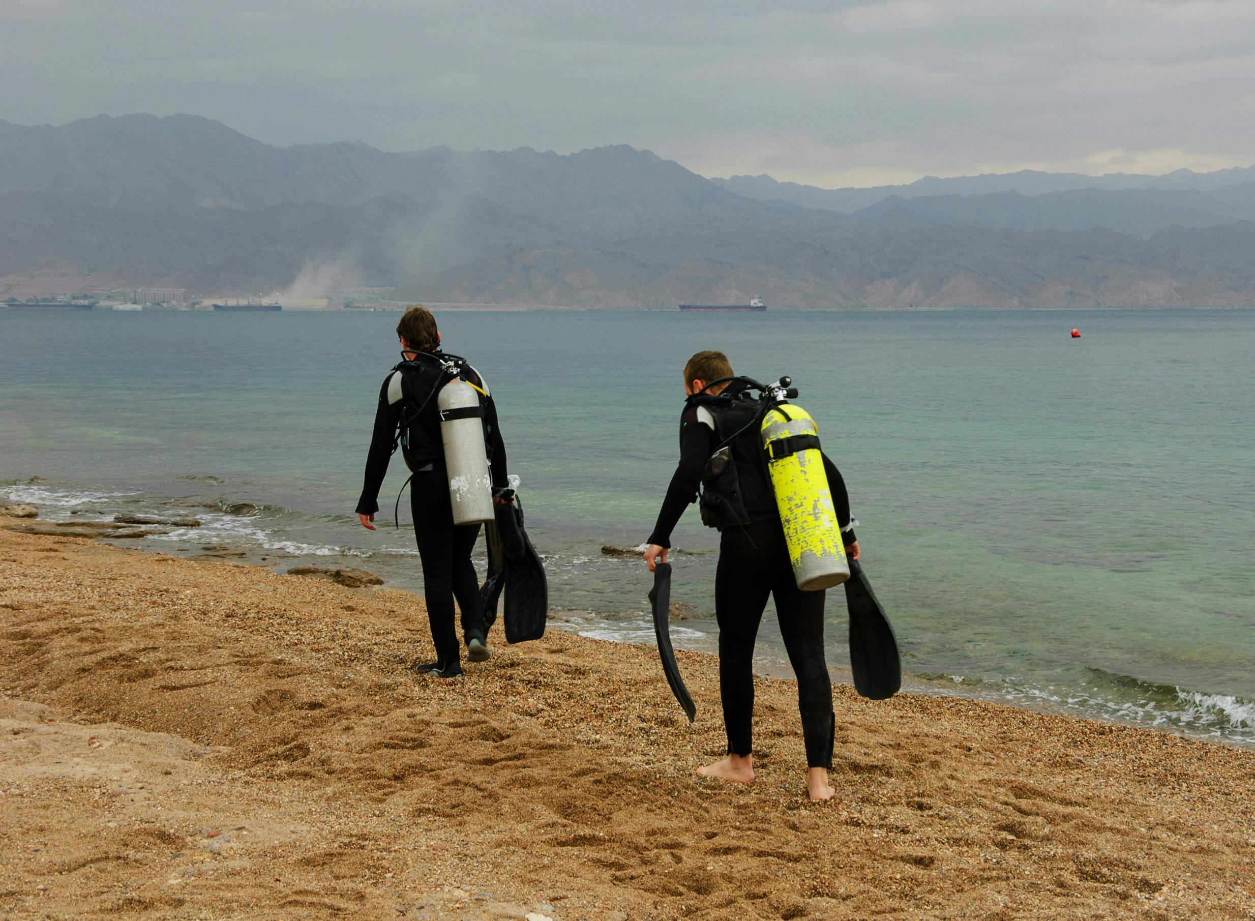 Two scuba divers walking along a shoreline