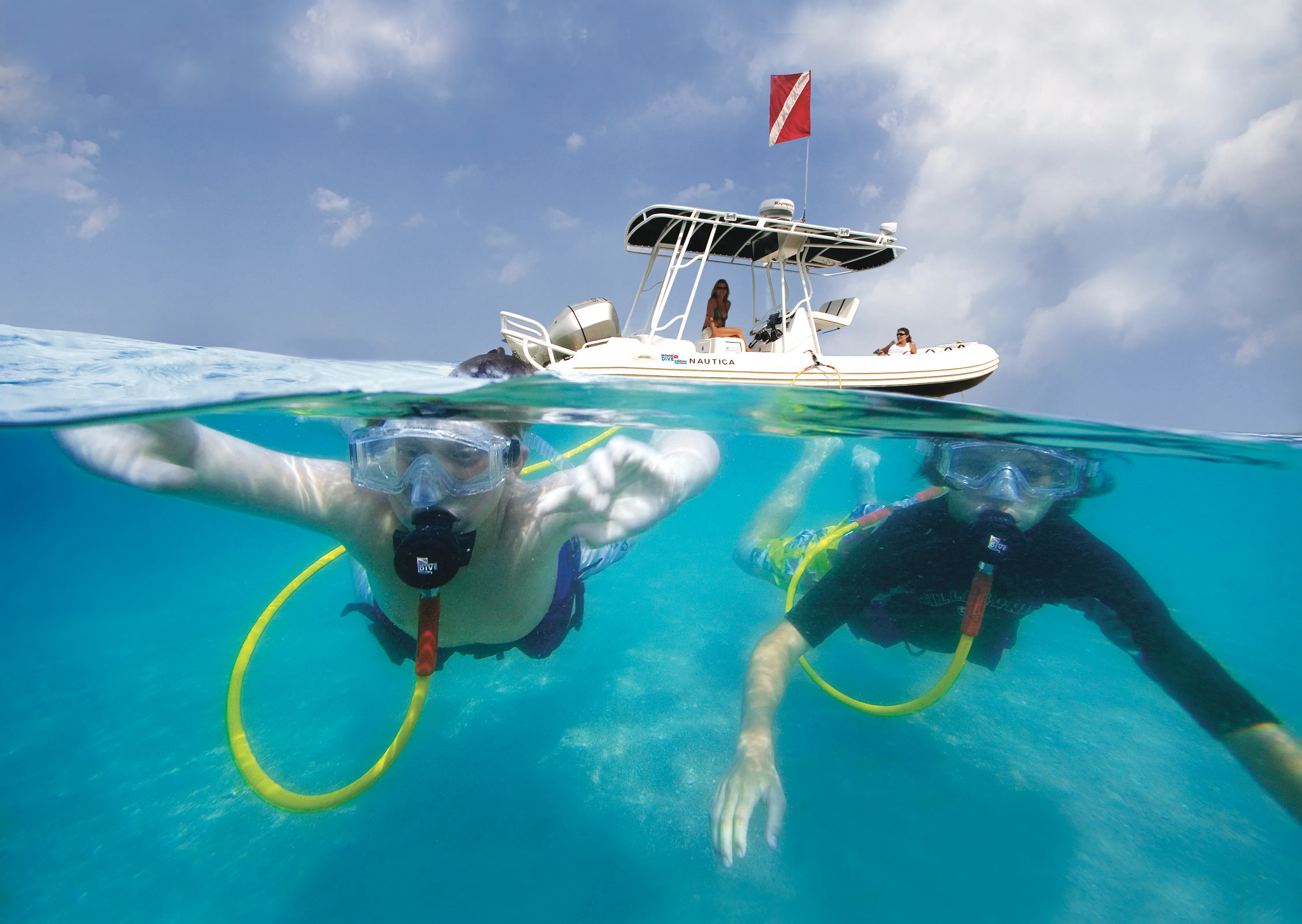 two divers using the hookah system near the ocean's surface. 50/50 shot with boat in the back and divers underwater