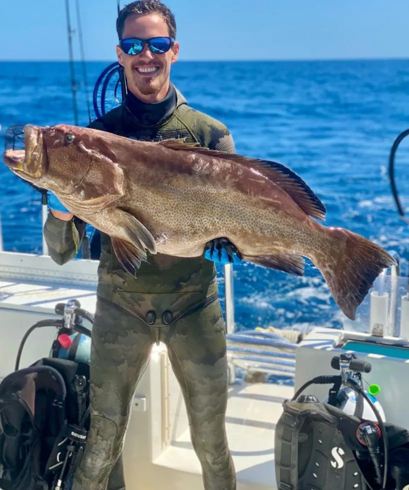 Spearfisherman holding large fish on vessel