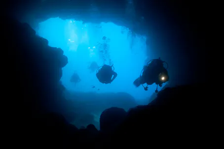 scuba divers heading into cavern with dive light in hand