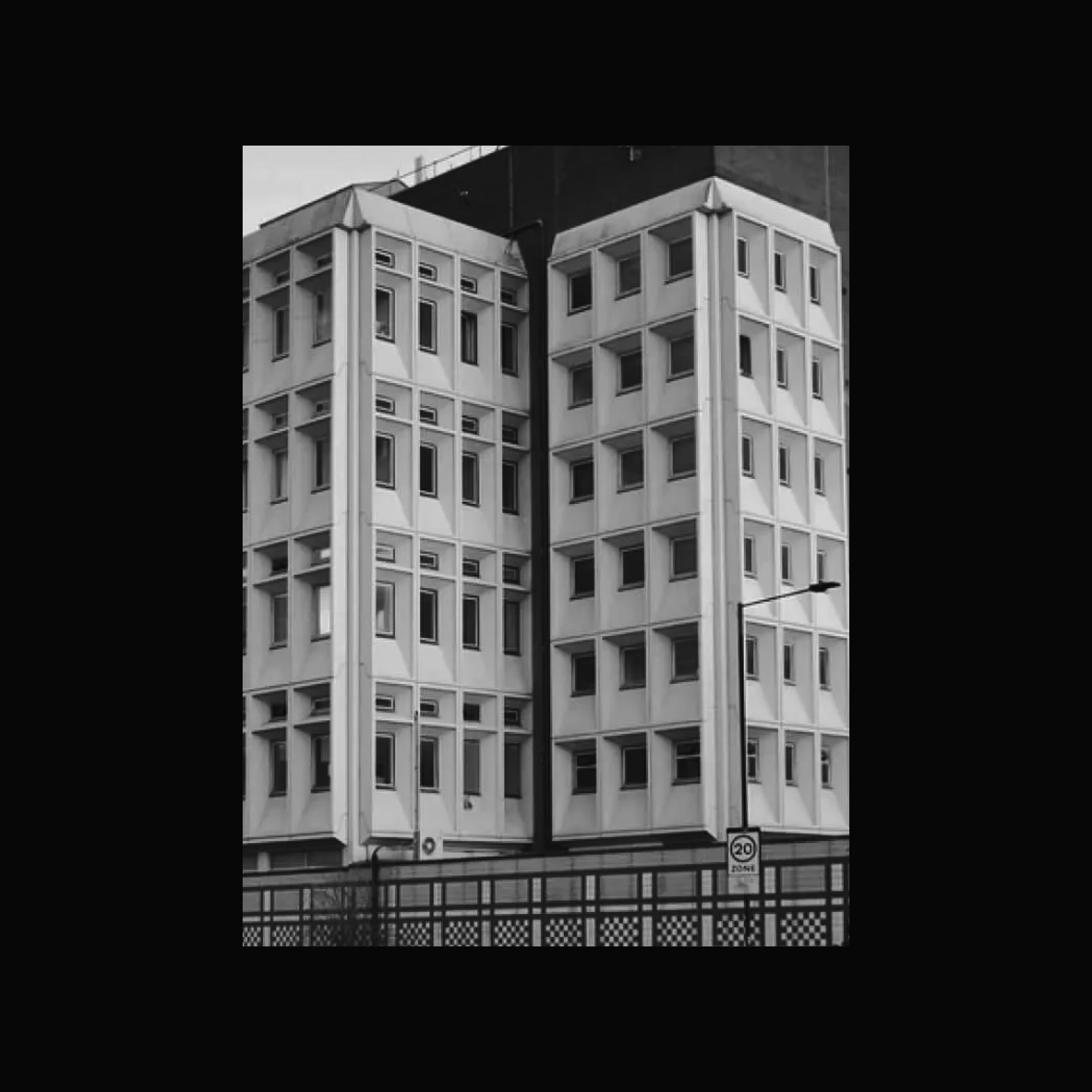 A black and white photo of a large, boxy building with many windows. The building is several stories tall and has a flat roof. 