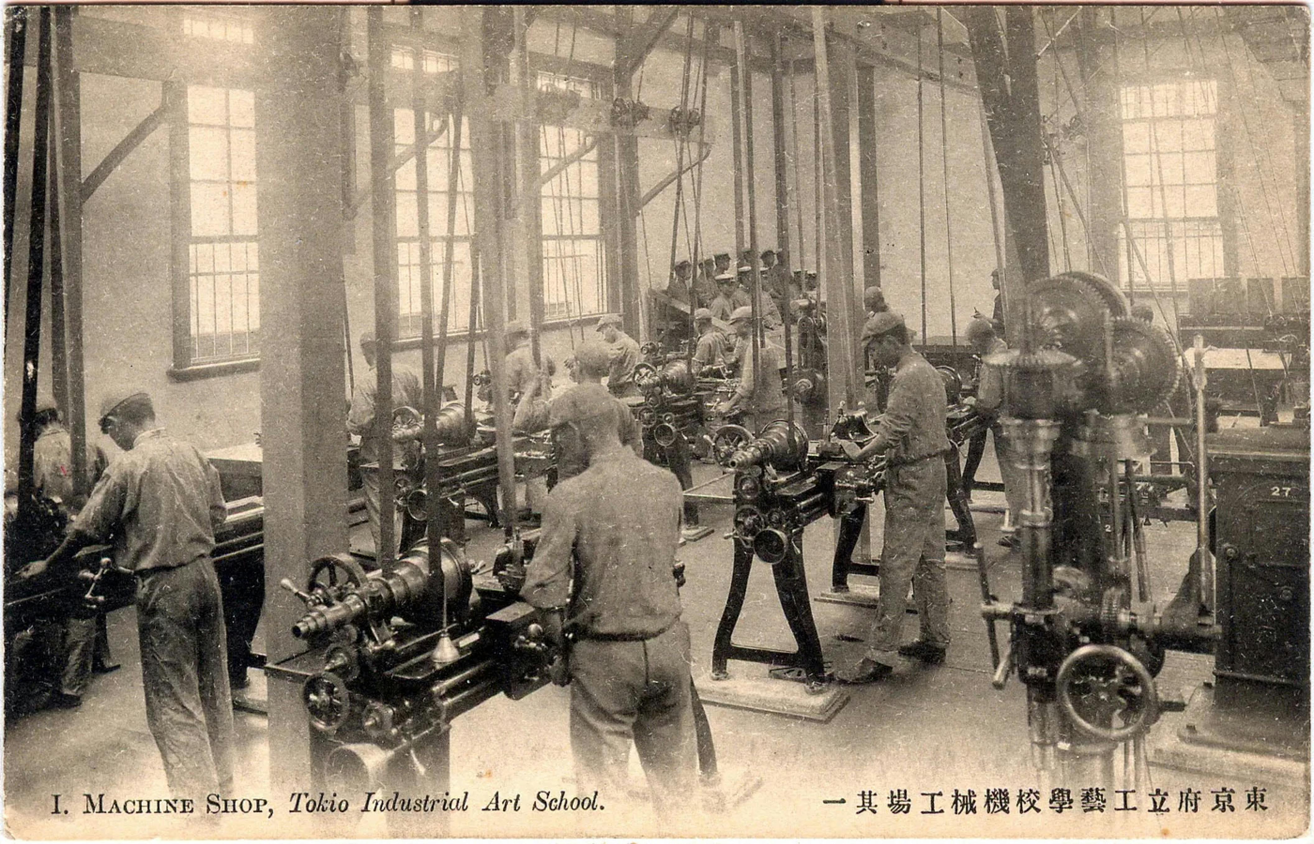 A black and white photo of a machine shop in the Tokyo Industrial Art School. Several students in uniform are working at various machines.

