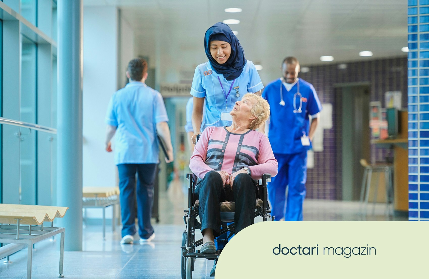 Eine Krankenschwester schiebt eine Patientin im Rollstuhl über einen Krankenhausflur.