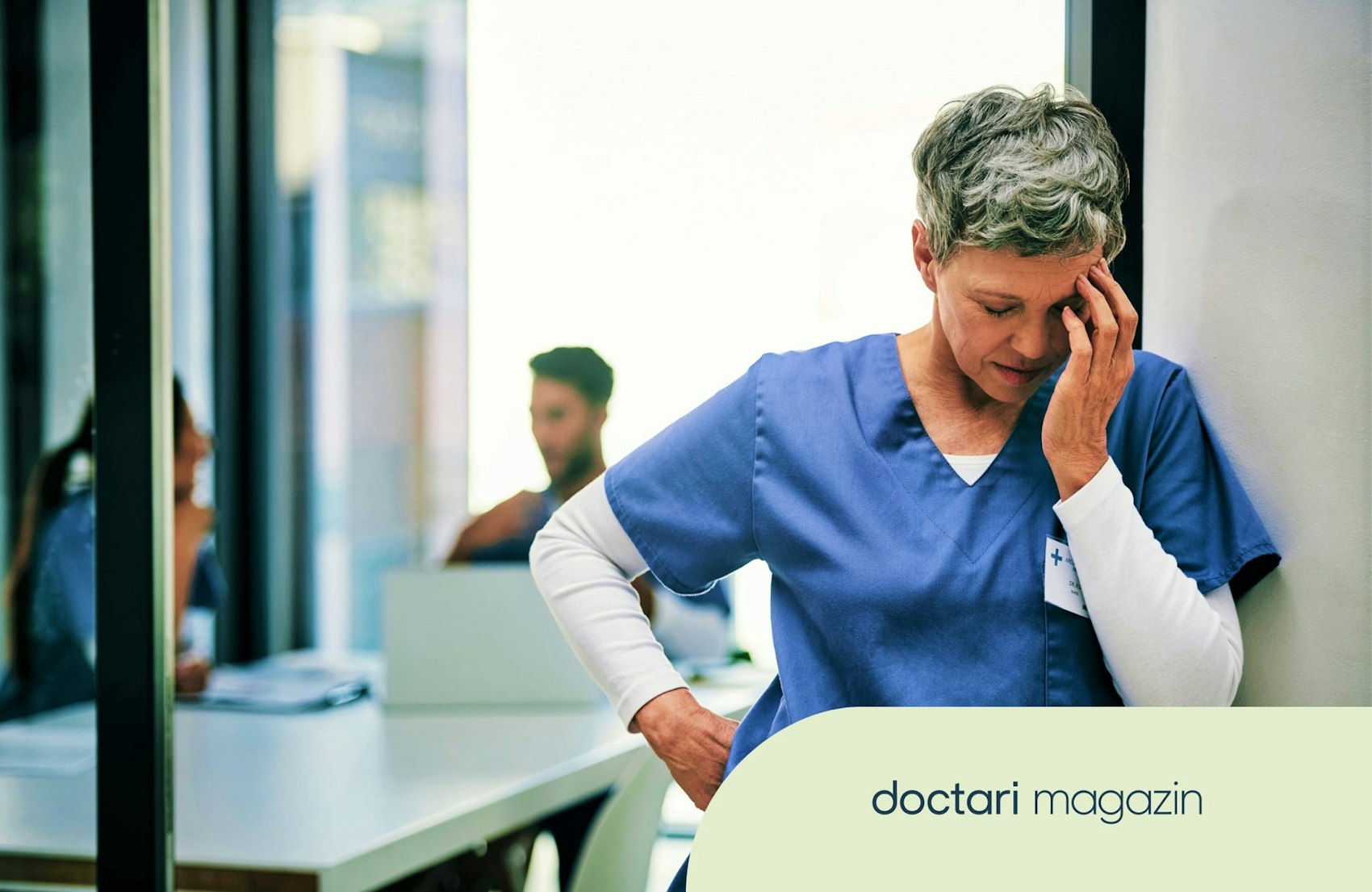 Eine gestresst wirkende Krankenpflegerin lehnt an der Wand und fasst sich an den Kopf.