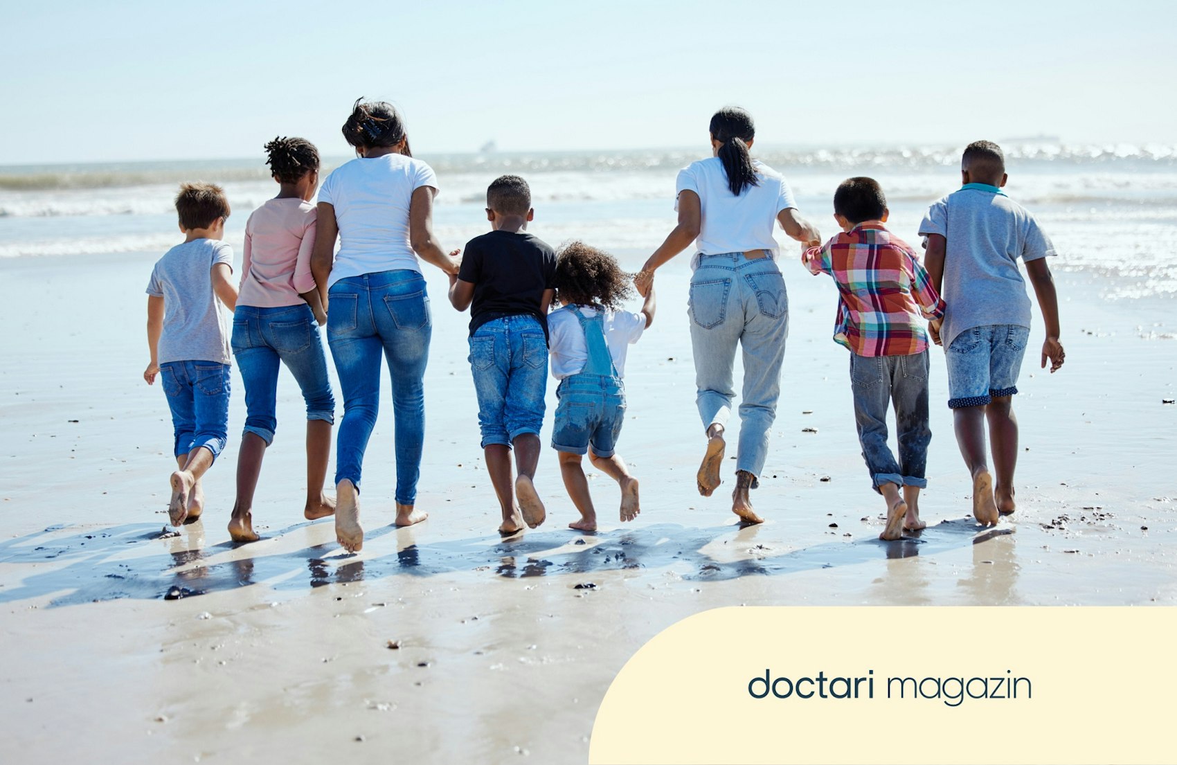 Zwei Erwachsene und sechs Kinder halten sich an den Händen und laufen am Strand entlang.
