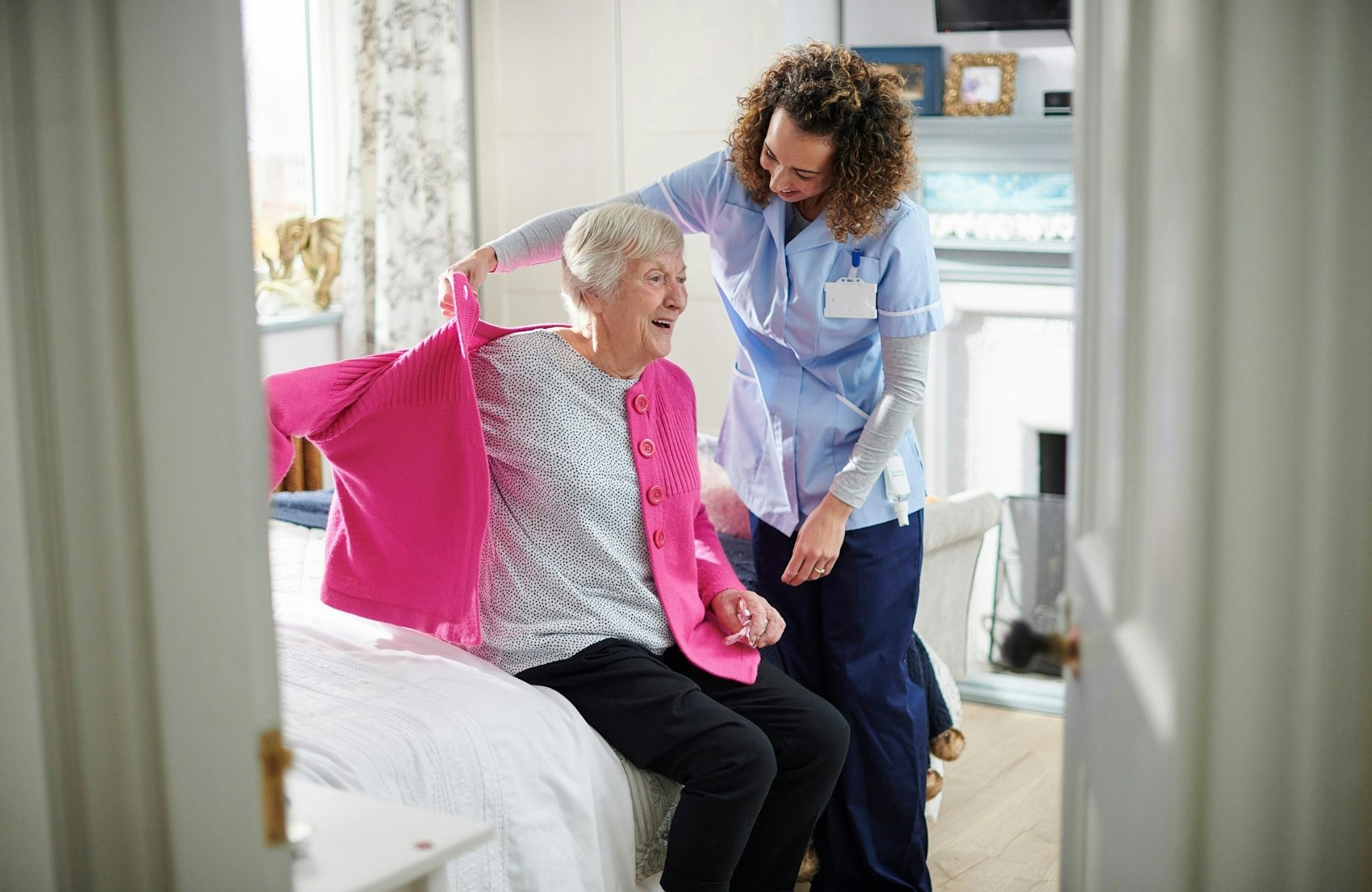 Altenpflegerin hilft zu pflegender Person dabei, ihre Strickjacke anzuziehen