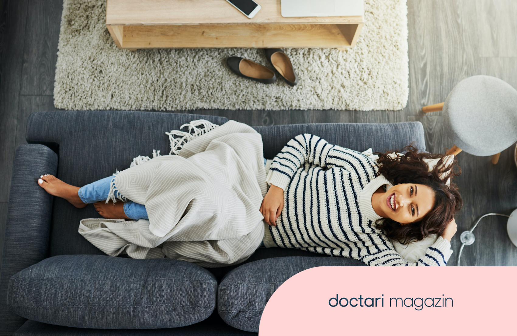 Junge Frau liegt auf einem Sofa und lacht in die Kamera.