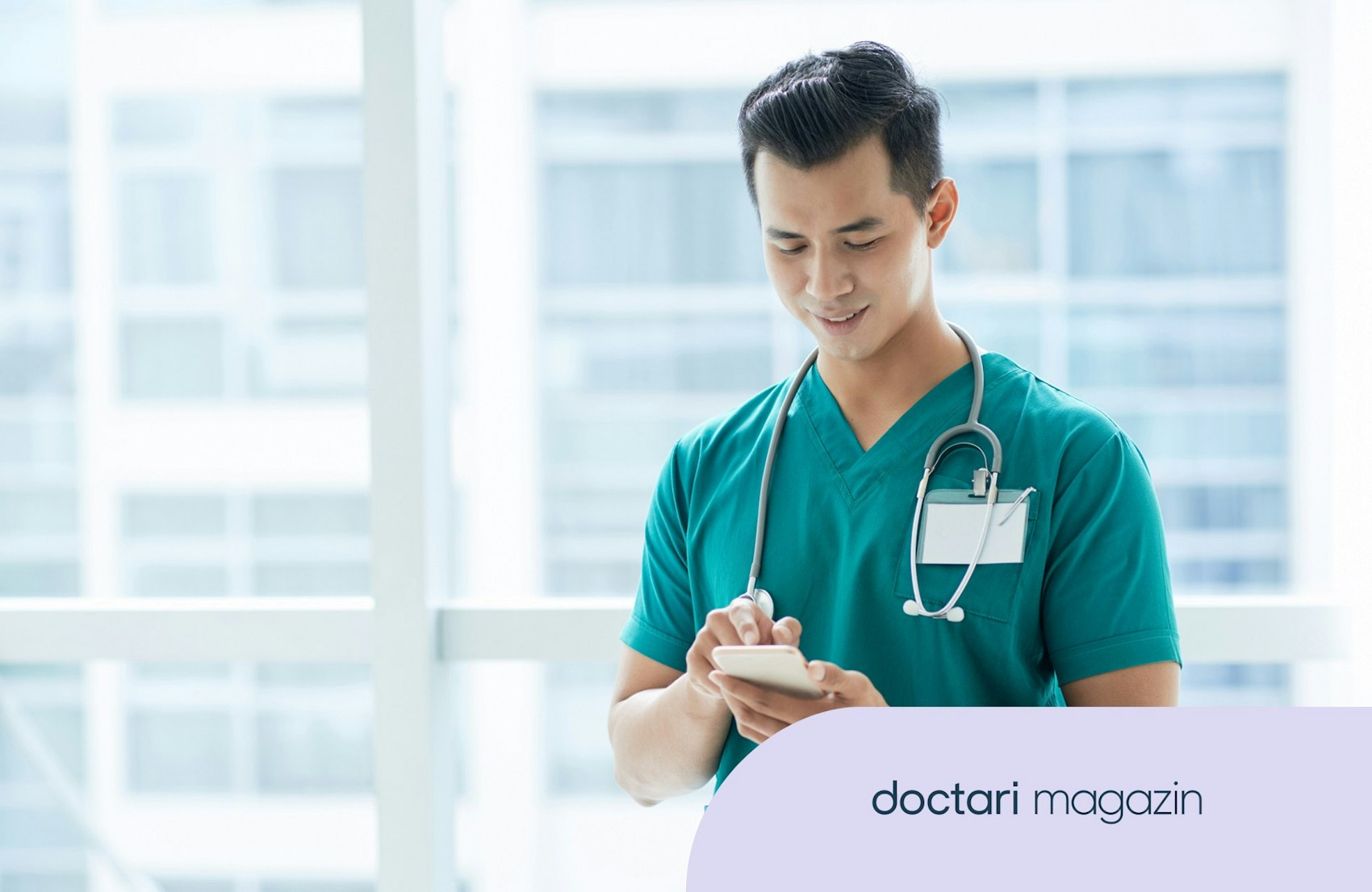 Ein junger Arzt im Kasak blickt auf sein Smartphone.