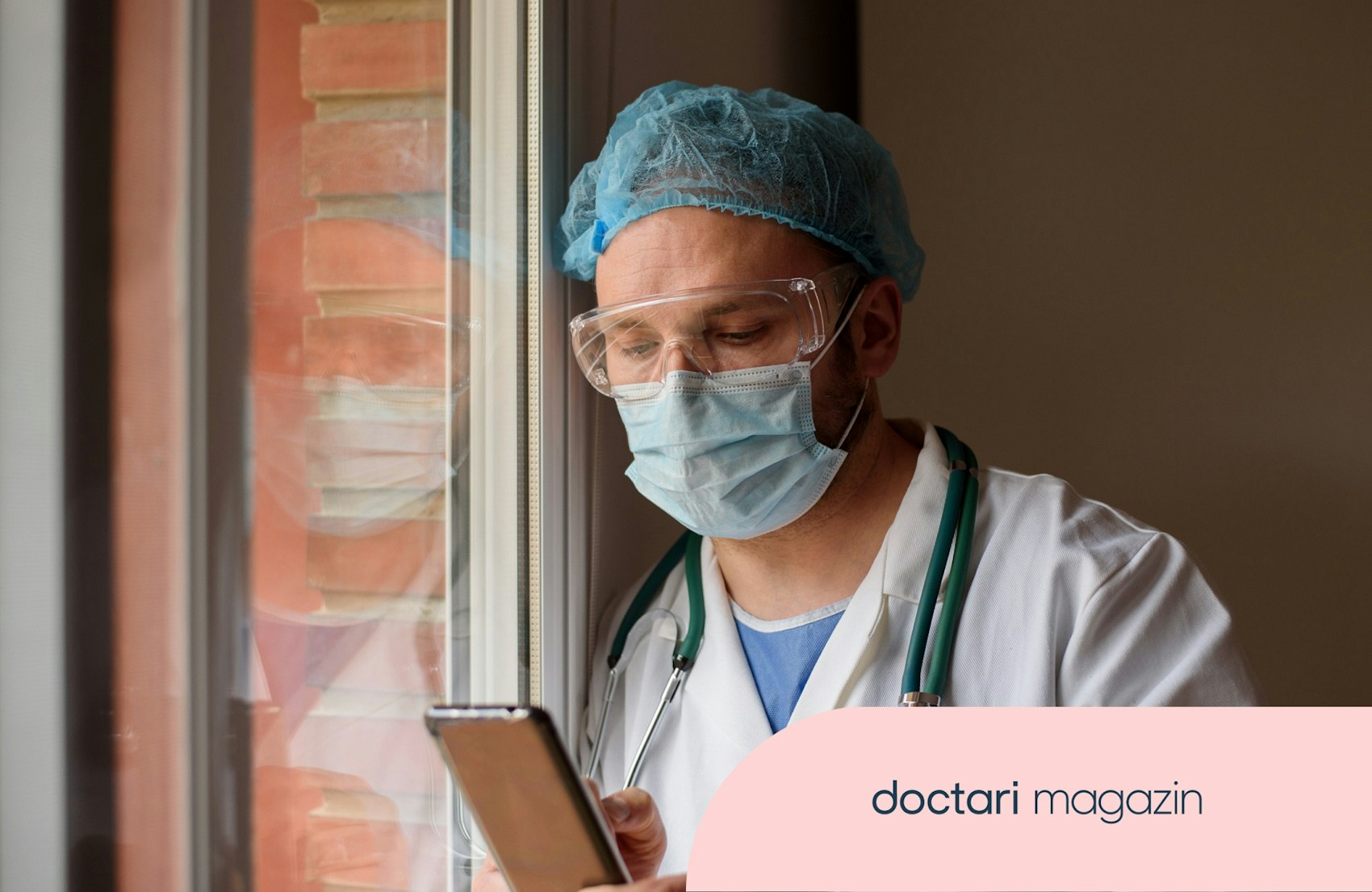 Ein Arzt mit Mundschutz und Haube blickt nachdenklich auf sein Smartphone.