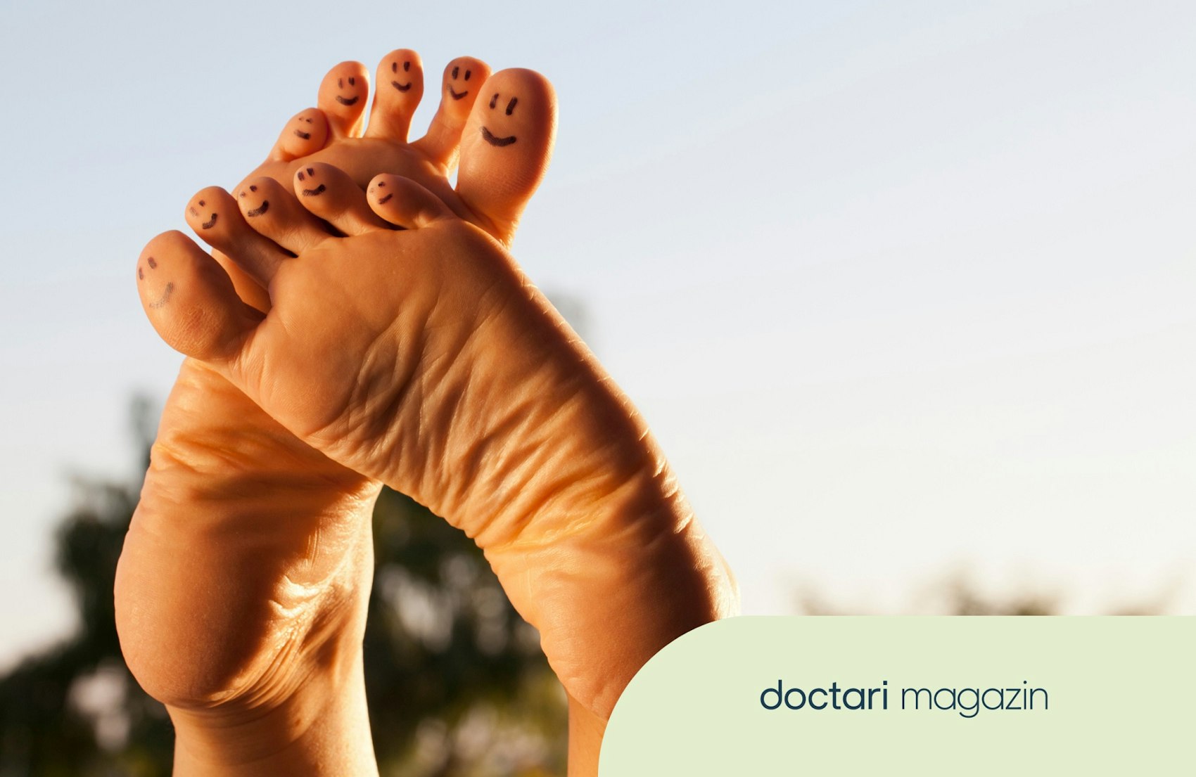 Zwei nackte Füße werden in die Luft gestreckt. Auf den Zehen sind mit Gesichter aufgemalt.