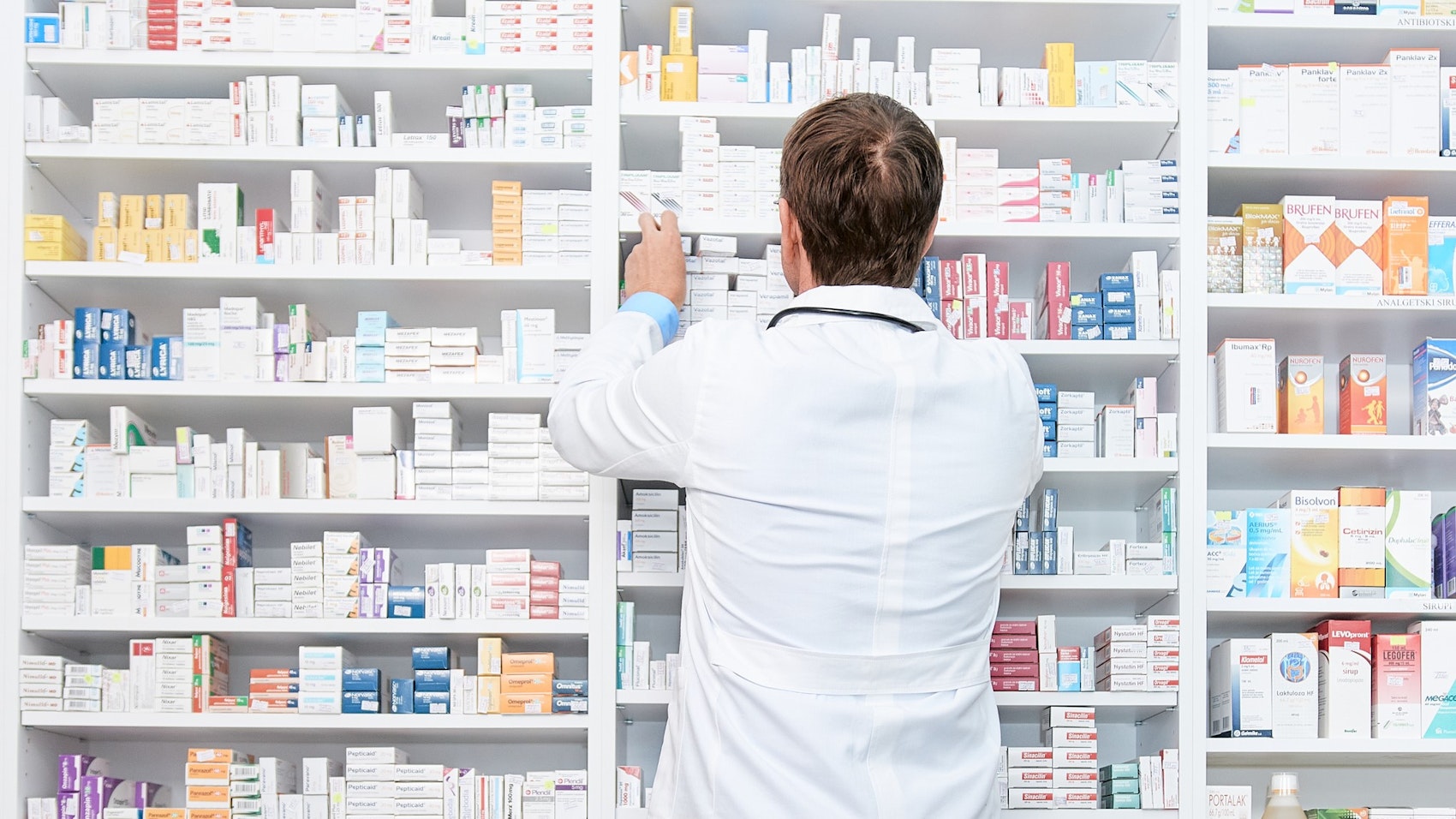 Ein Apotheker nimmt Tabletten aus einem großen Regal mit Medikamenten.