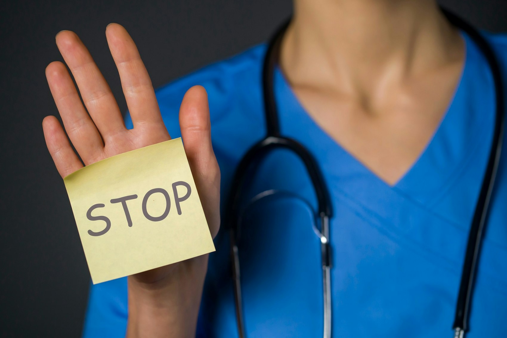 Eine medizinische Fachkraft in Kasack hält ein Post-it in die Kamera auf dem "Stop" steht.