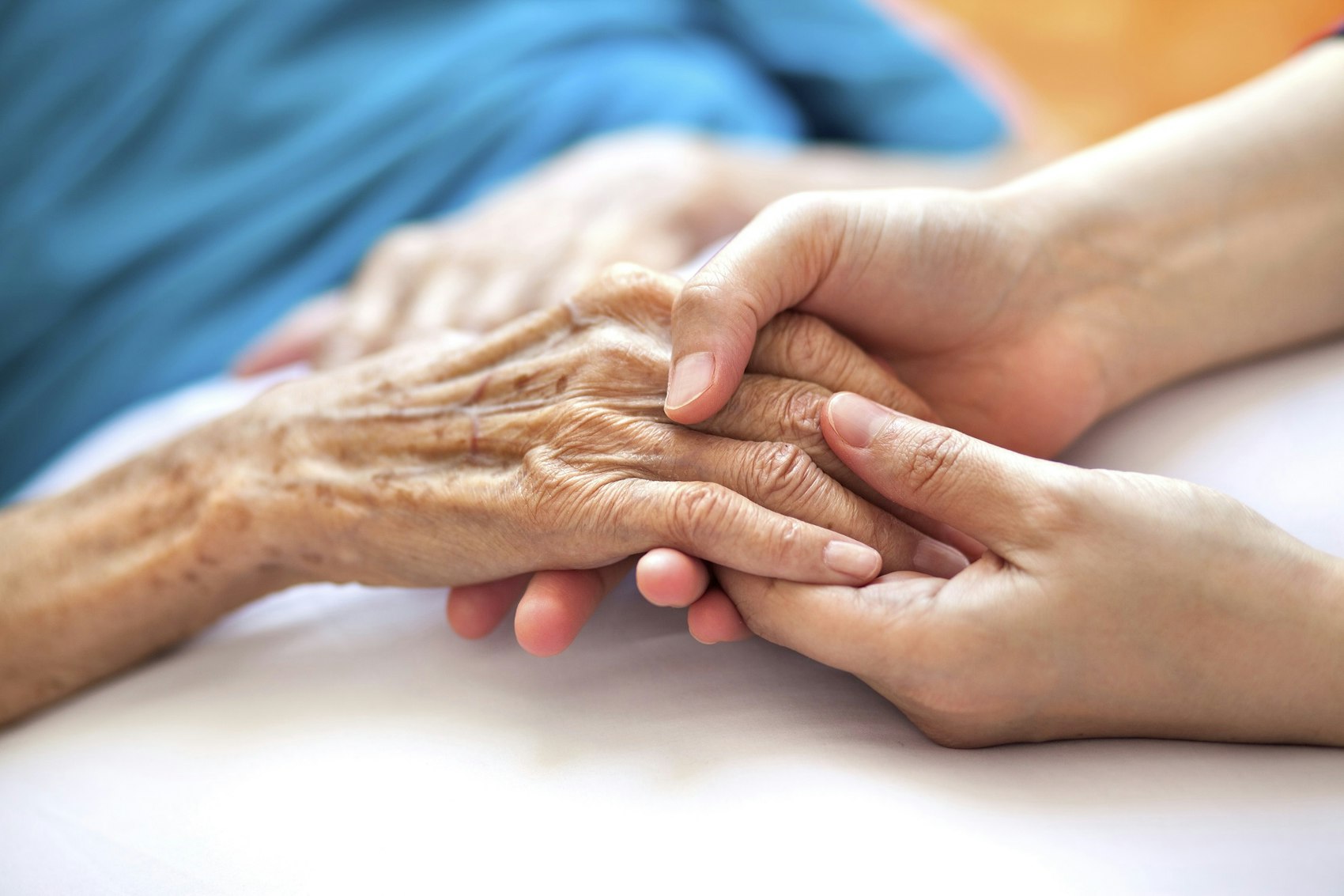 Zwei Hände einer jungen Frau halten die Hand einer Seniorin.