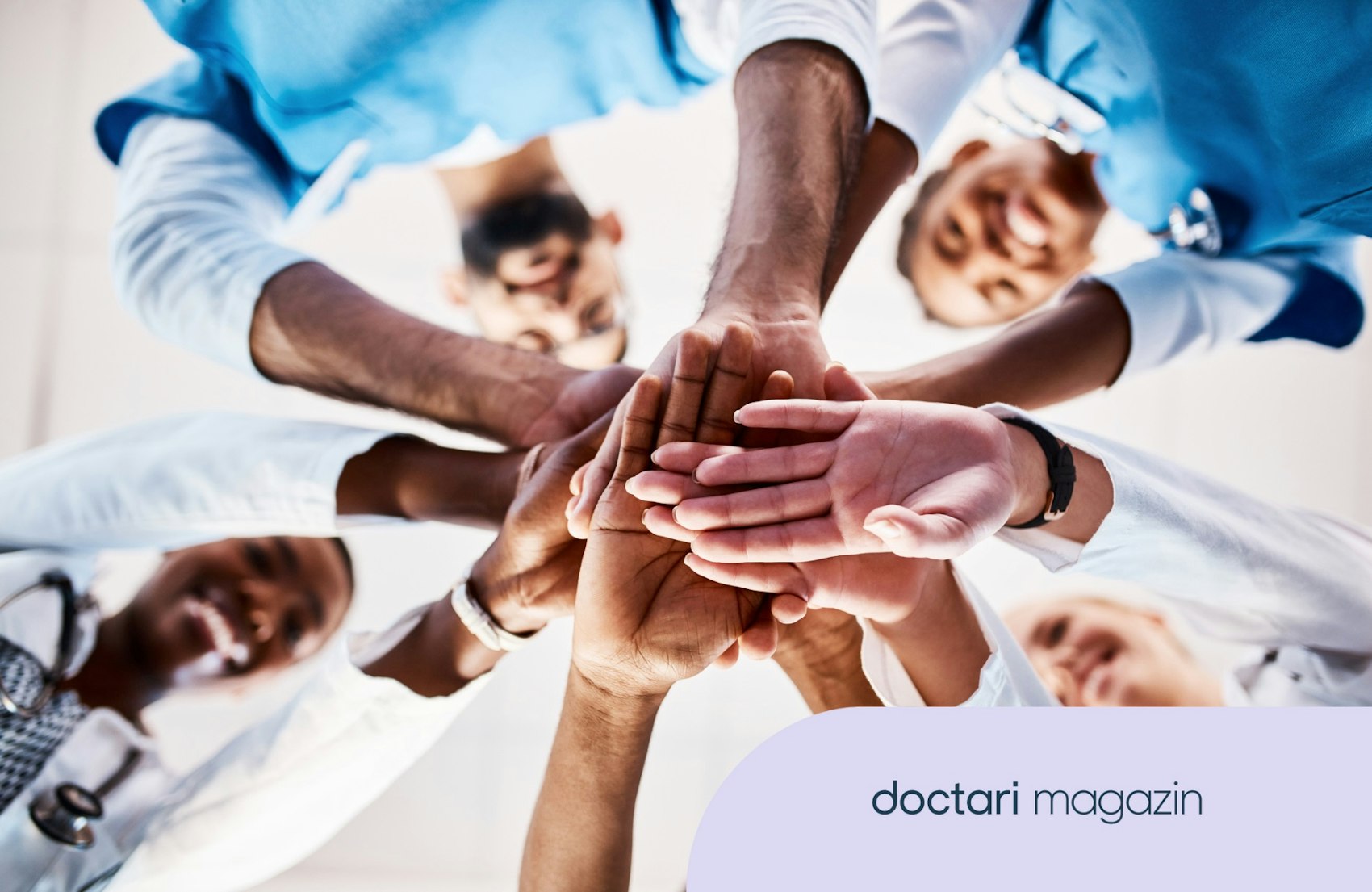 Mehrere Ärzte stehen im Kreis und legen ihre Hände in der Mitte aufeinander.