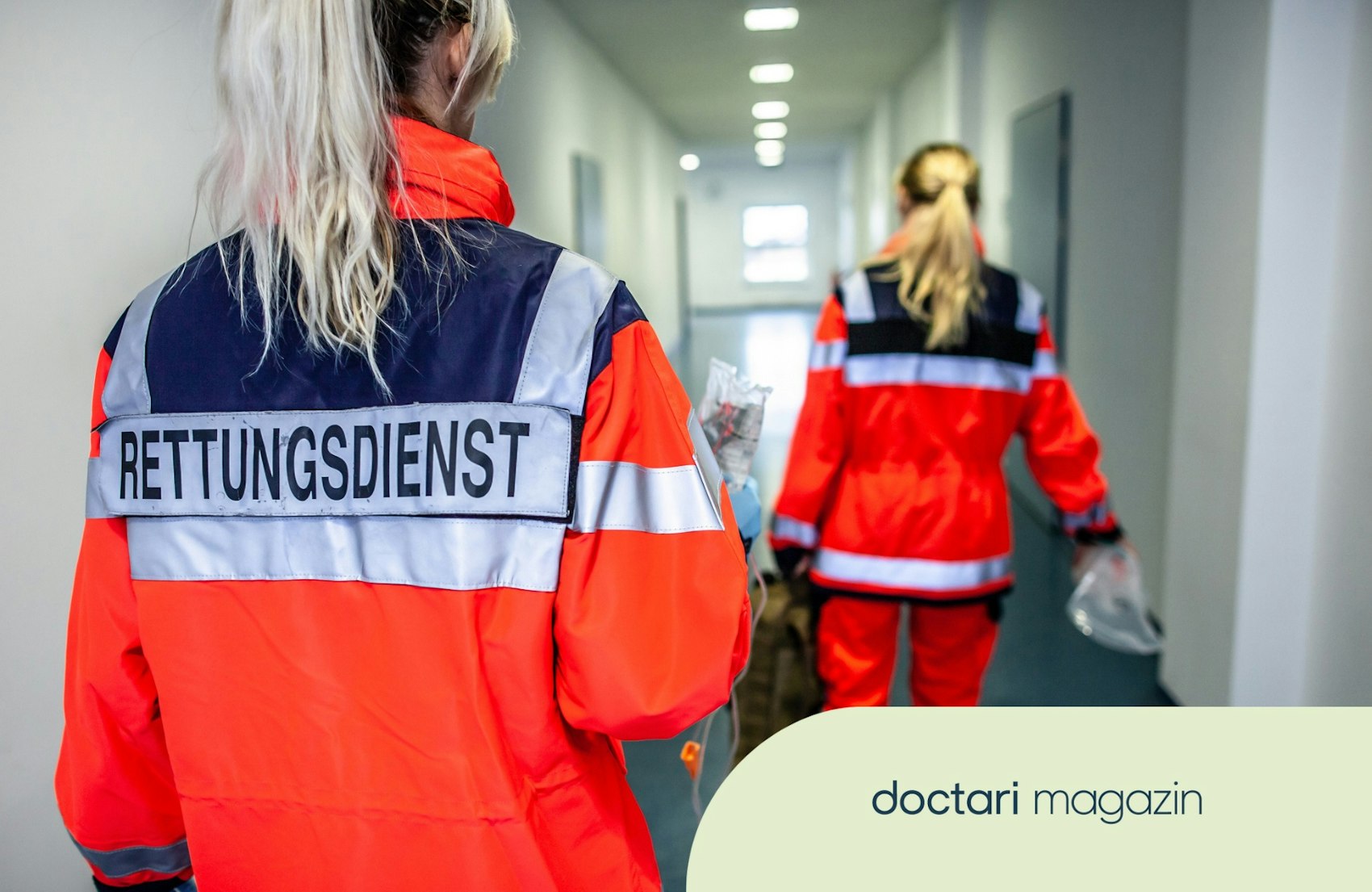 Zwei Rettungskräfte laufen einen Flur entlang. Die Schrift "Rettungsdienst" steht hinten auf einer der Jacken.