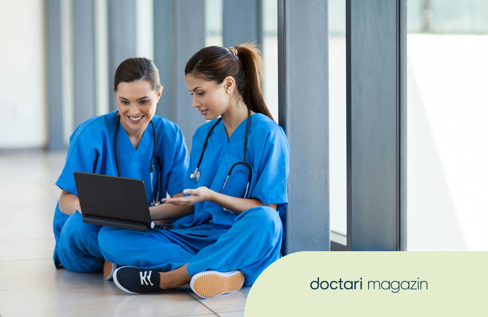 Zwei Pflegekräfte sitzen gemeinsam auf dem Boden eines Krankenhausflurs.