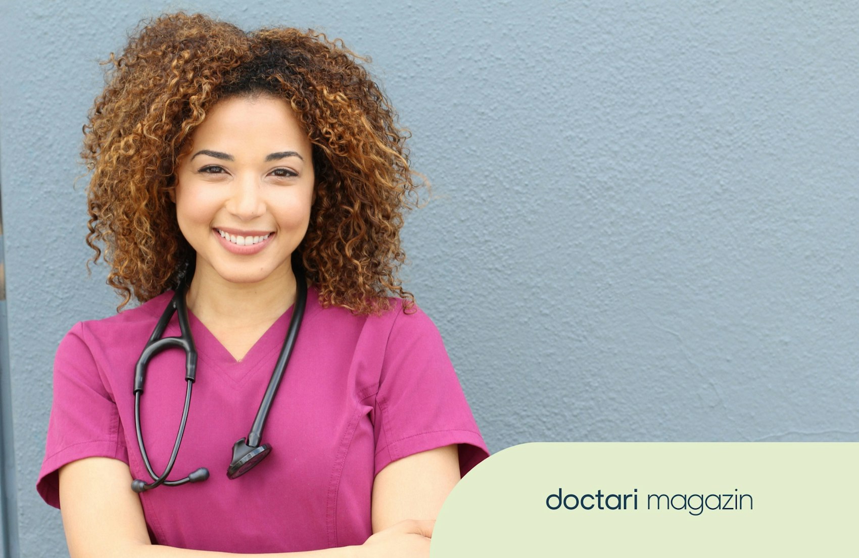 Eine junge Pflegefachfrau im pinkfarbenen Kasak lächelt in die Kamera.