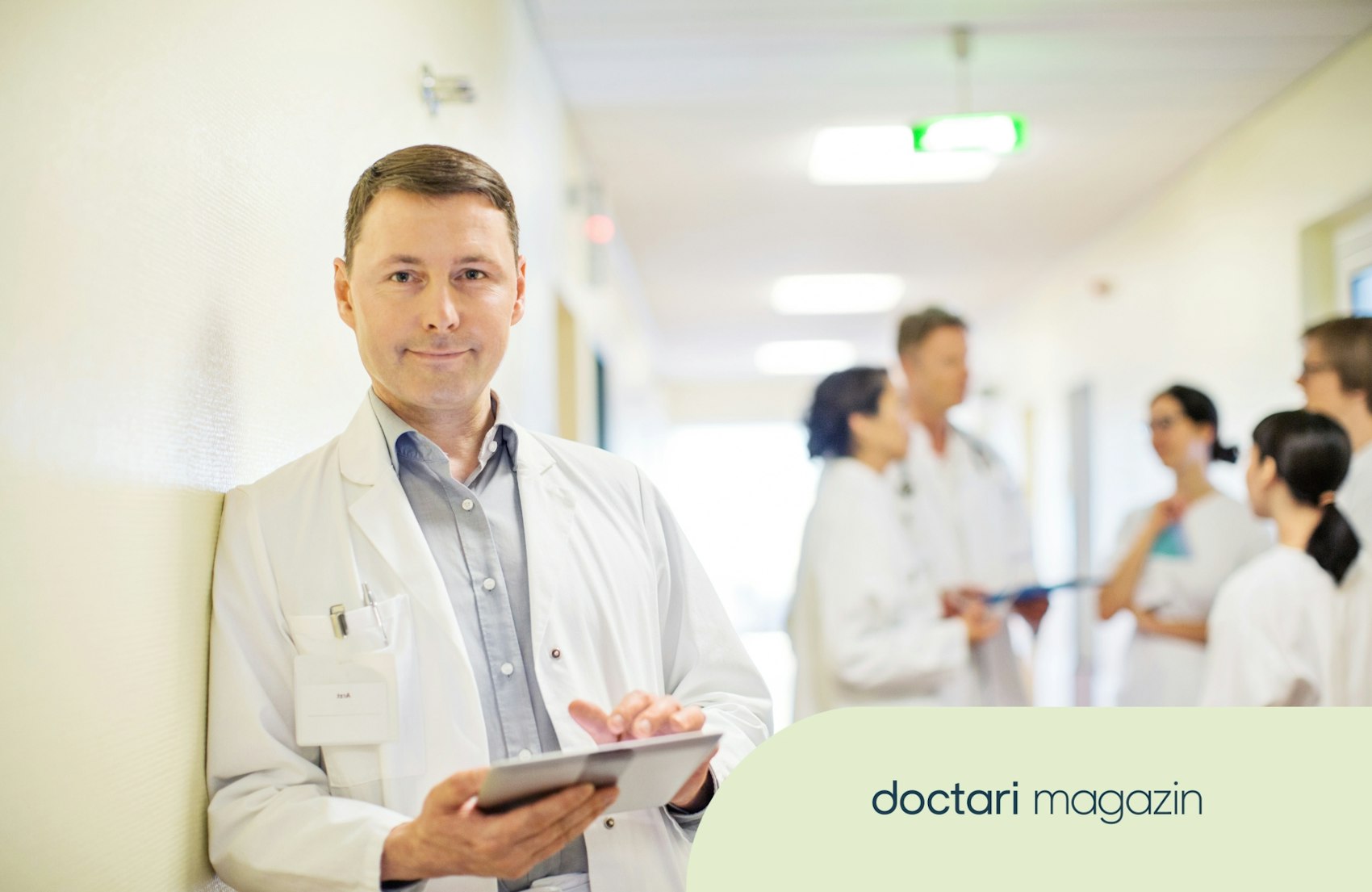 Arzt mit Klemmbrett guckt freundlich, KollegInnen im Hintergrund