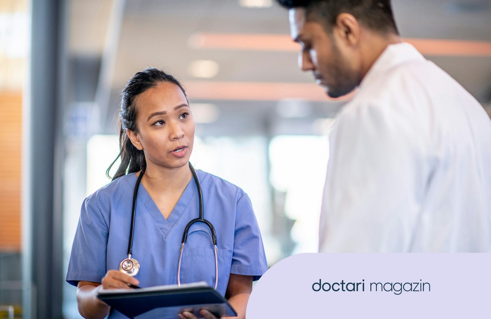 Junge Ärztin spricht auf dem Krankenhausflur mit einem Kollegen.