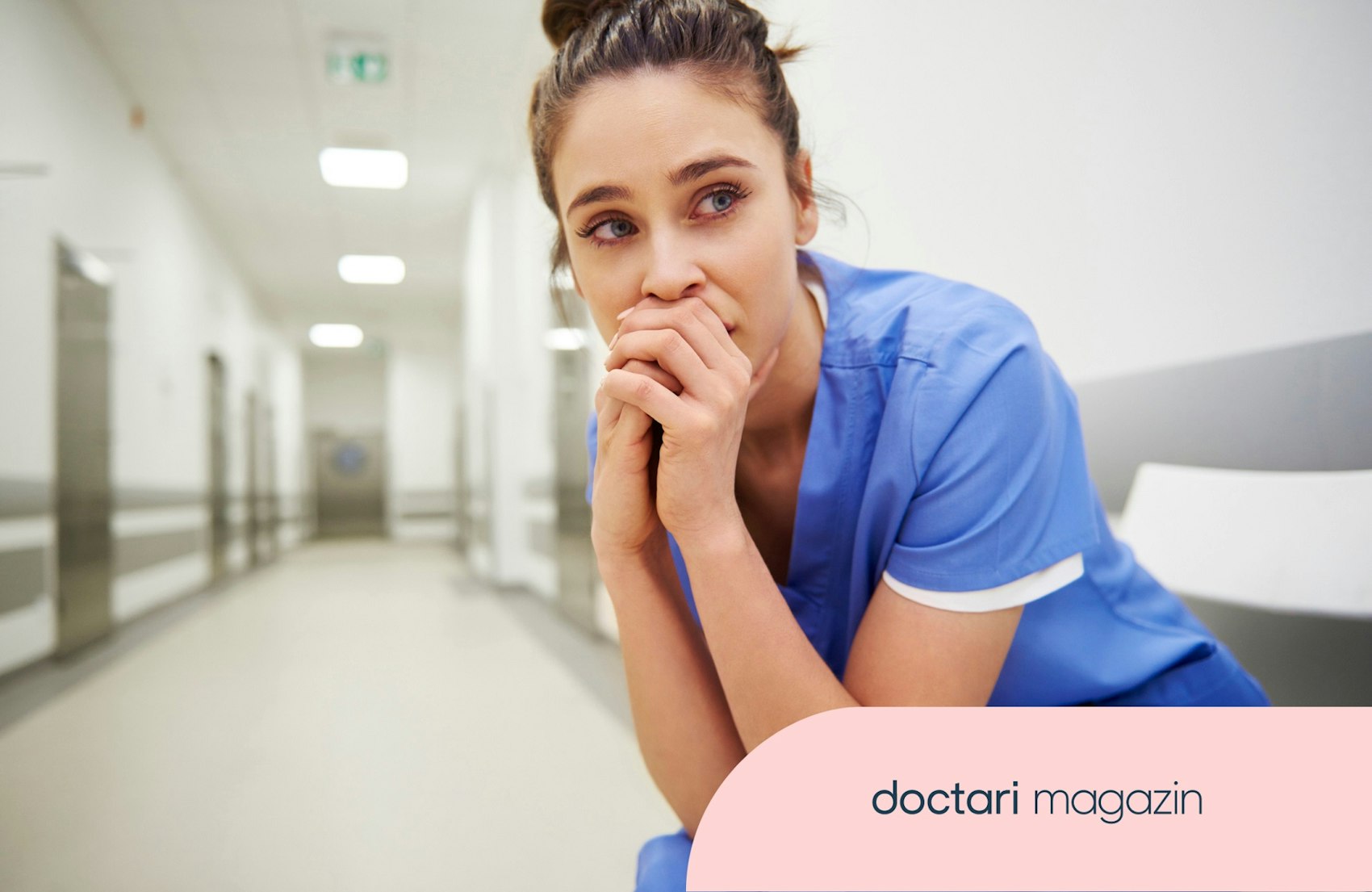 Besorgt blickende junge Ärztin sitz auf einem Stuhl in einem Krankenhausflur.