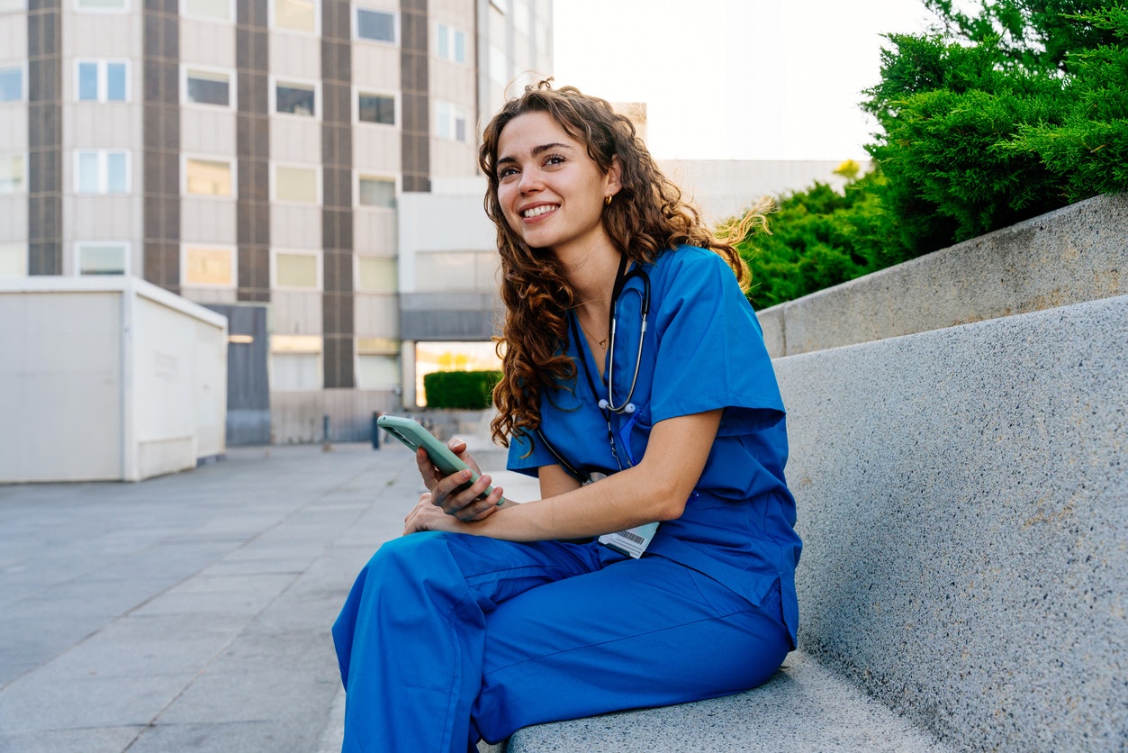 Eine junge Pflegekraft macht gerade Pause vor einem Krankenhaus
