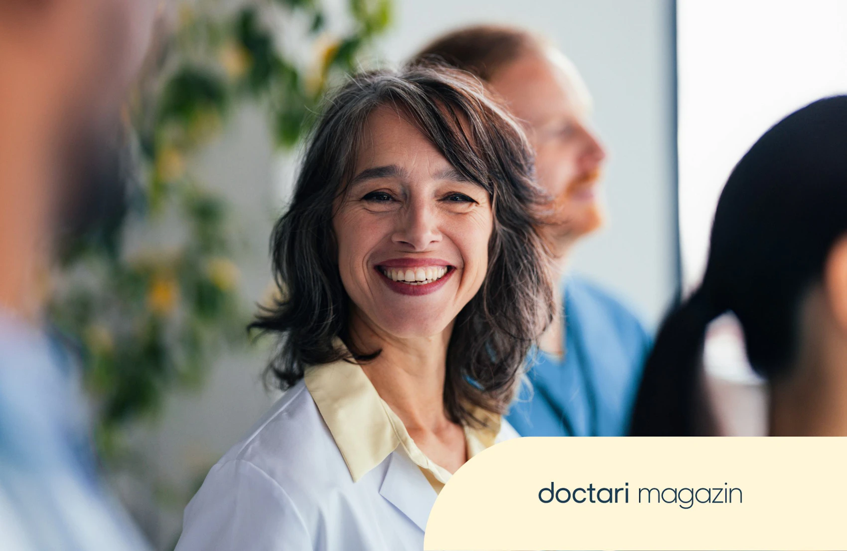 Lächelnde Ärztin mit Kollegen im Krankenhauskorridor, positiver Teamgeist im Gesundheitswesen