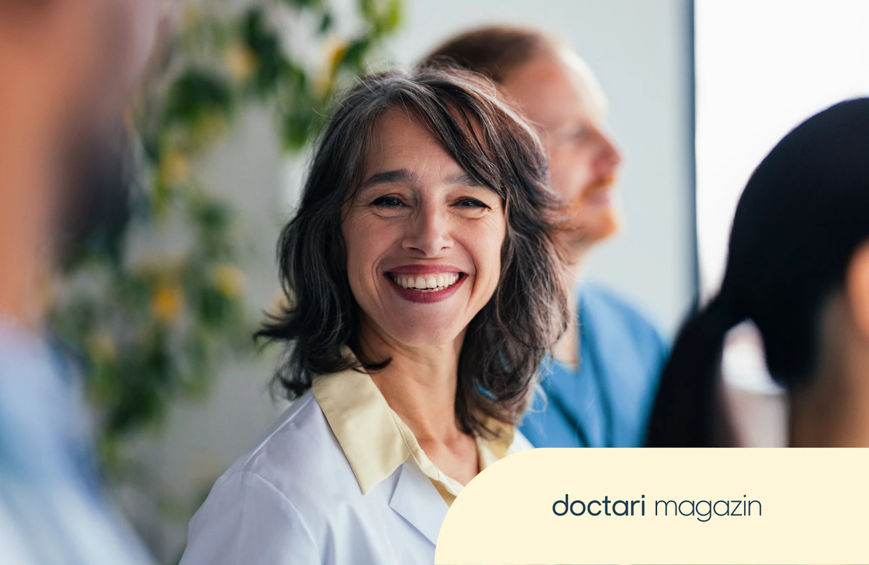 Lächelnde Ärztin mit Kollegen im Krankenhauskorridor, positiver Teamgeist im Gesundheitswesen