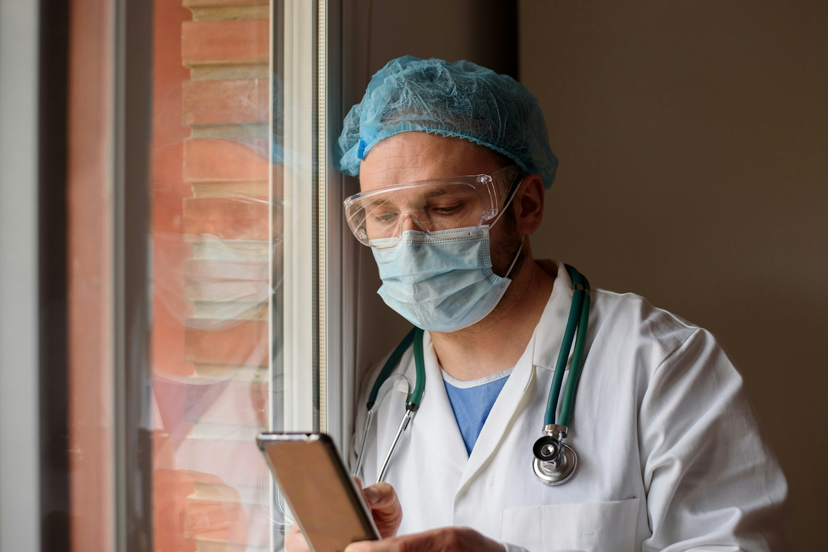 Ein Arzt mit Haube und Stethoskop blickt auf sein Smartphone
