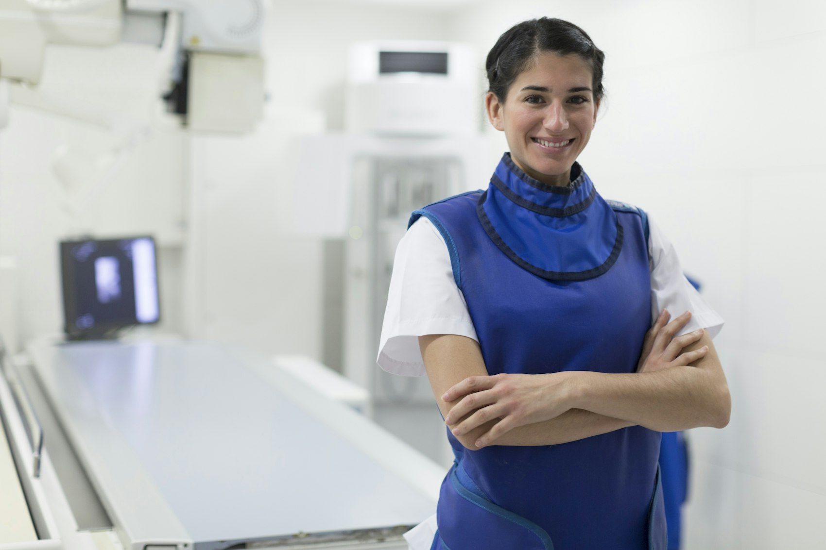Eine lächelnde MTRA mit Bleischürze steht vor einem Röntgengerät