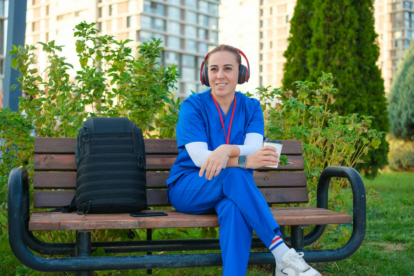 Eine junge Pflegerin sitzt in ihrer Pause auf einer Parkbank und hört Podcasts